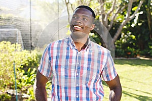 Happy african american man standing in sunny garden smiling