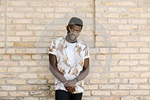 Happy African American man in sunglasses stands near a brick building on the street on a sunny day. Close-up portrait