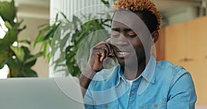 Happy african american man talking by phone while using laptop computer in cafe