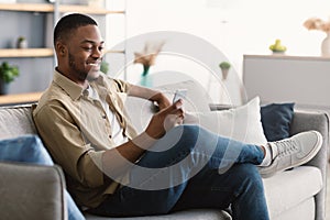 Happy African American Man Using Phone Texting Sitting At Home