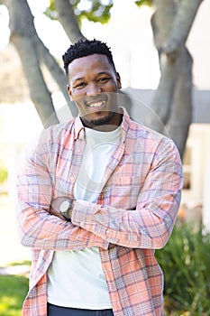 Happy african american man walking with arms crossed in sunny garden, copy space