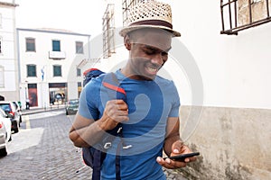 Happy african american man walking outdoors in the city with cellphone and bag