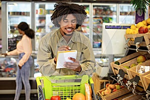Happy African American Man Writing Grocery Shopping List In Supermarket