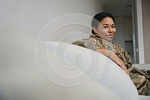 Happy african american military woman is sitting in bright living room