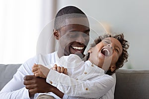 Happy african american millennial father tickling laughing son.