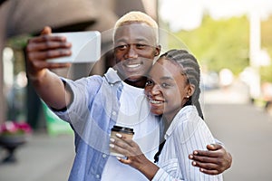 Happy african american millennial guy and girl with coffee, hugs and maks selfie