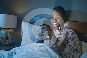 Happy African American millennial woman as social media addict - night lifestyle portrait of young beautiful and cool black girl