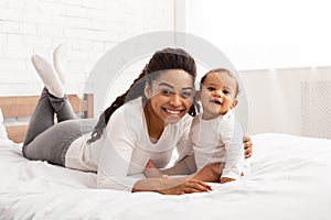 Happy African American Mom Embracing Baby Boy Posing In Bedroom