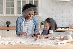 Happy African American mom helping cute daughter to bake biscuit