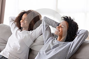 Happy african american mom and teen daughter relaxing on sofa