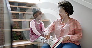 Happy african american mother advising and tying shoes of daughter at home, slow motion