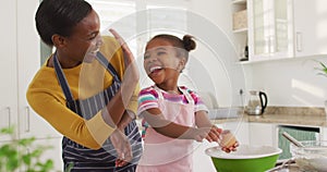 Happy african american mother and daughter cooking and giving high five in kitchen