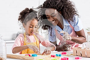 happy african american mother and daughter making cookies with cookie cutters together