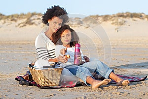 Happy African American mother and daughter on picnic on beach