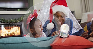 Happy african american mother with daughter playing with snow globe