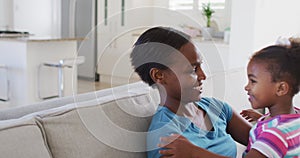 Happy african american mother and daughter sitting on sofa and hugging