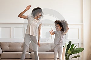 Happy african american mother doing morning exercises with excited daughter.