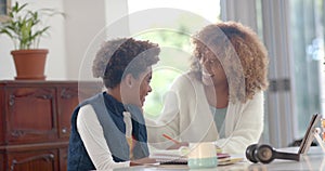 Happy african american mother helping her son with homework using tablet in kitchen, slow motion