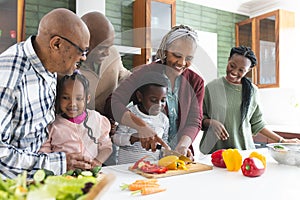 Happy african american multi generation family chopping vegetables in kitchen, slow motion