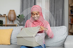 Happy african american muslim woman opening delivery box and looking inside, unboxing parcel with purchases