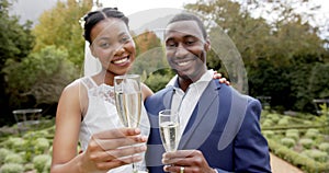 Happy african american newlyweds toasting with champagne at their wedding in garden, slow motion