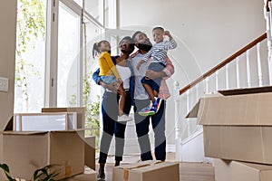 Happy african american parents carrying children with key by cardboard boxes in new home, copy space