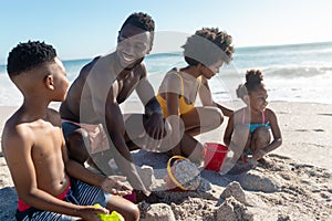 Happy african american parents and children making sandcastles together at beach on sunny day