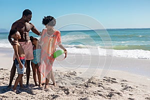 Happy african american parents and children standing together with ball at beach on sunny day