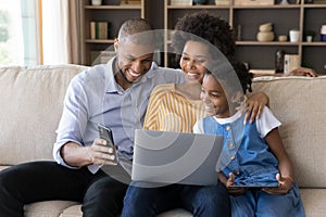 Happy African American parents and daughter kid resting on couch