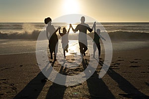 Happy african american parents enjoying sunset with children at beach against sky