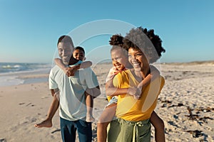 Happy african american parents giving piggyback to children while walking at beach on sunny day