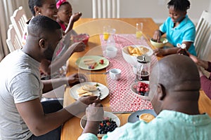 Happy african american parents, grandparents and grandchildren sitting at table eating