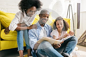 happy african american parents and little daughter reading book together