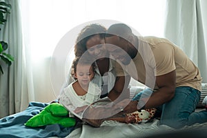 Happy African American Parents with little daughters playing , reading book on the bed in bedroom at home, happy family concept