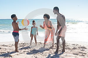 Happy african american parents playing ball with children at beach on sunny day