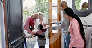 Happy african american parents, son and daughter welcoming grandparents at front door, slow motion
