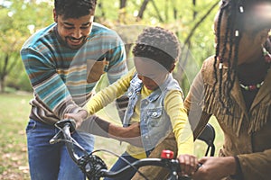 Happy African American parents teaching their little girl to driving bike in park.