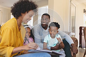 Happy African American parents with their cute children reading storybook on the sofa