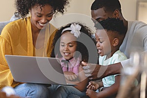 Happy African American parents with their cute children using laptop on sofa