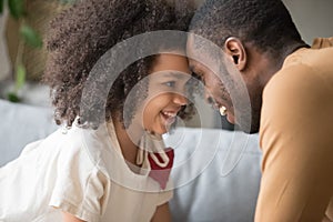 Happy African American preschool daughter and father touching foreheads