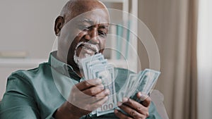 Happy african american satisfied winning bet elderly retired man counting savings mature male with pile dollars counting