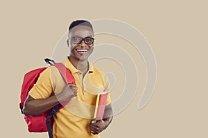 Happy African American student with bag and books standing on beige copy space background