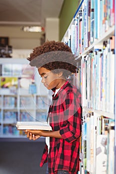 Happy african american schoolboy reading book standing in school library