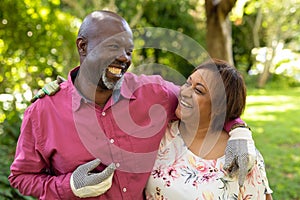 Happy african american senior couple with arms around gardening in backyard