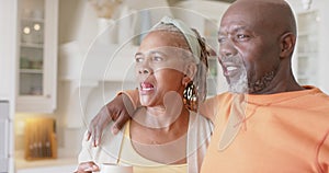 Happy african american senior couple embracing and drinking coffee in kitchen, slow motion