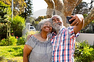 Happy african american senior couple taking selfie in garden