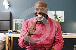 Happy african american senior man making video call smiling and giving thumb up sign to camera