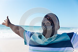 Happy african american senior retired man with eyes closed and arms outstretched at beach