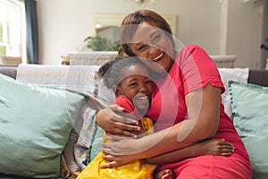 Happy african american senior woman embracing granddaughter on sofa at home