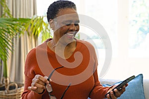 Happy african american senior woman with glasses, using smartphone in sunny living room, copy space